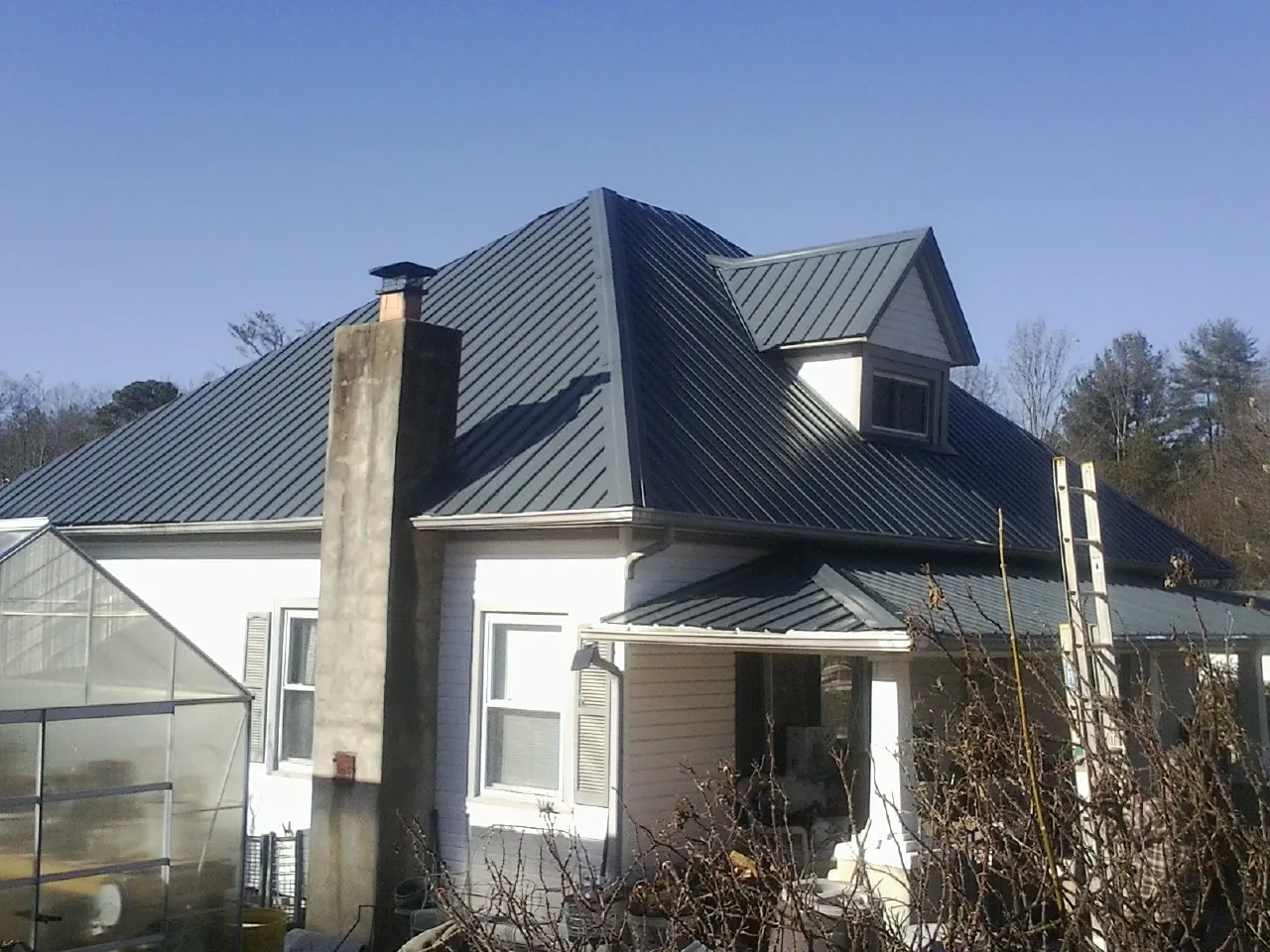 Dark blue standing seam metal roof on a white farmhouse with dormer — Slate & Tile Roof Repair by Roofing Brothers in Clawson