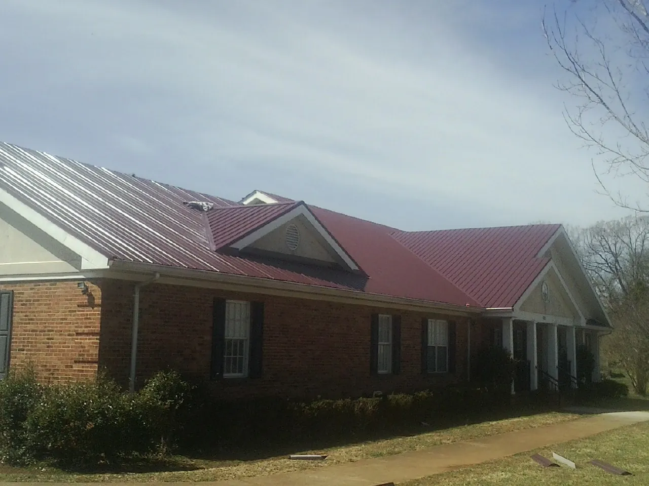 Red metal roof with gabled entries on a long brick building, from a Hail Damage Roof Repair job in Clawson