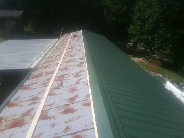 Old rusted panels beside newly installed green metal roofing — Wind Damage Roof Repair by Roofing Brothers in Clawson