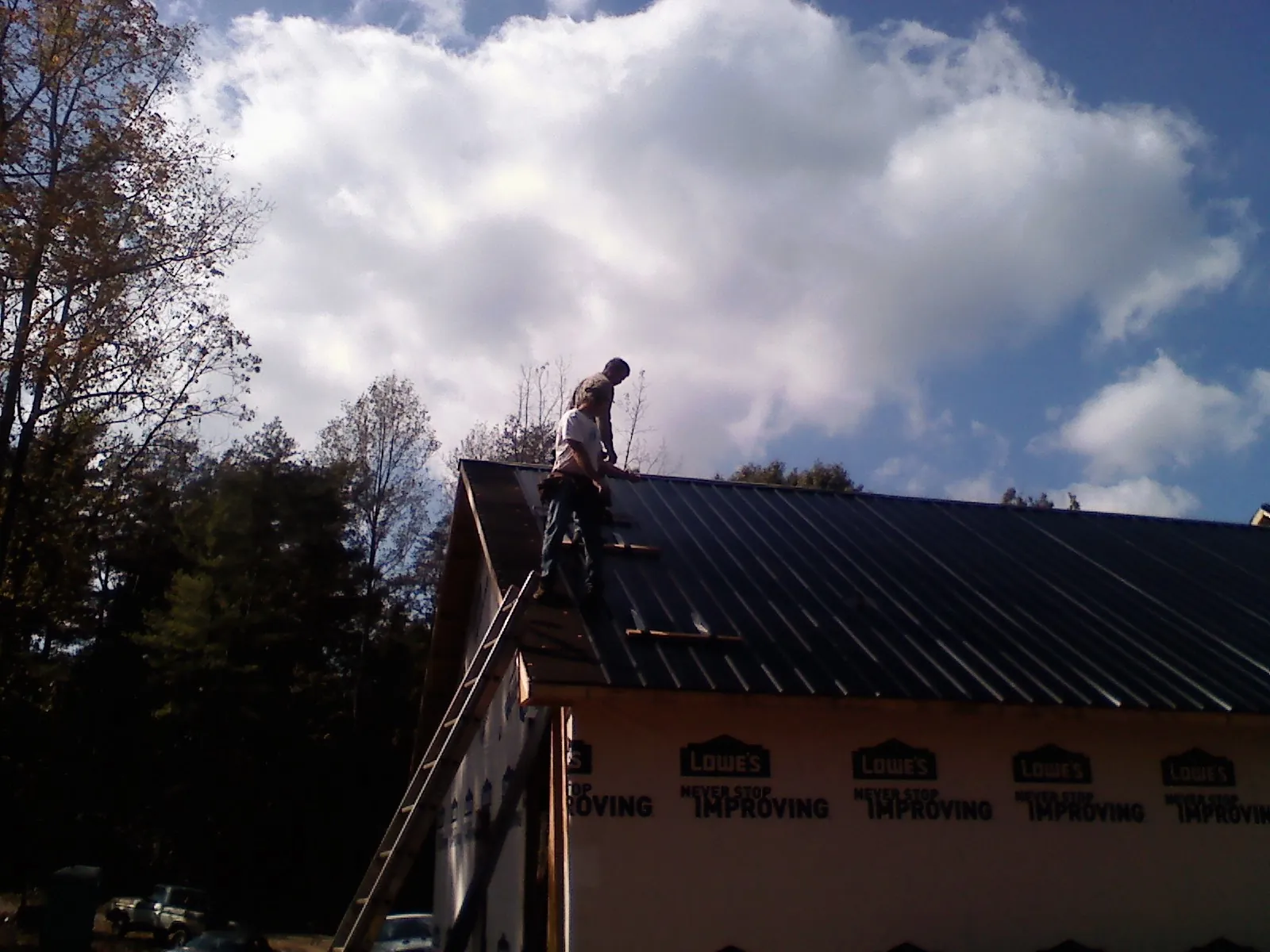 Roofer fastening dark metal panels high against a cloudy sky, from a Roof Inspection job in Clawson