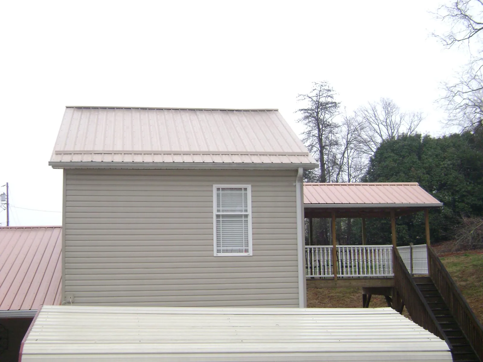Tan metal roofs on a two story addition and attached porch, from a Roof Replacement job in Clawson